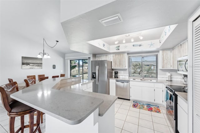 kitchen with light tile patterned flooring, a tray ceiling, a breakfast bar, white cabinets, and appliances with stainless steel finishes