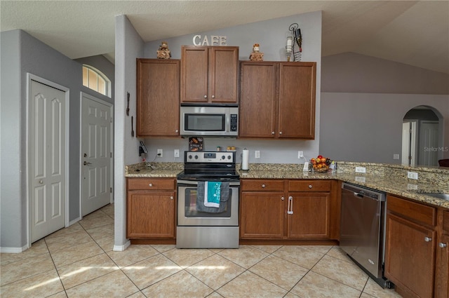 kitchen with light stone countertops, appliances with stainless steel finishes, light tile patterned floors, and vaulted ceiling