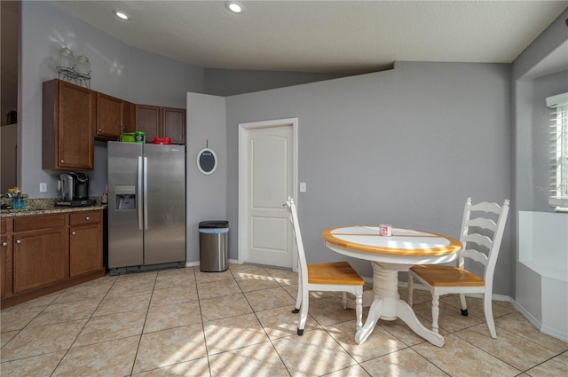 kitchen featuring stainless steel fridge with ice dispenser, light tile patterned flooring, light stone countertops, and vaulted ceiling