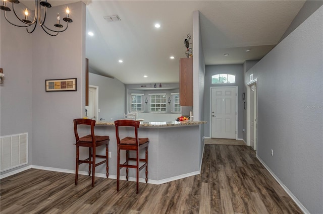 kitchen with dark hardwood / wood-style floors, kitchen peninsula, a chandelier, vaulted ceiling, and a breakfast bar area