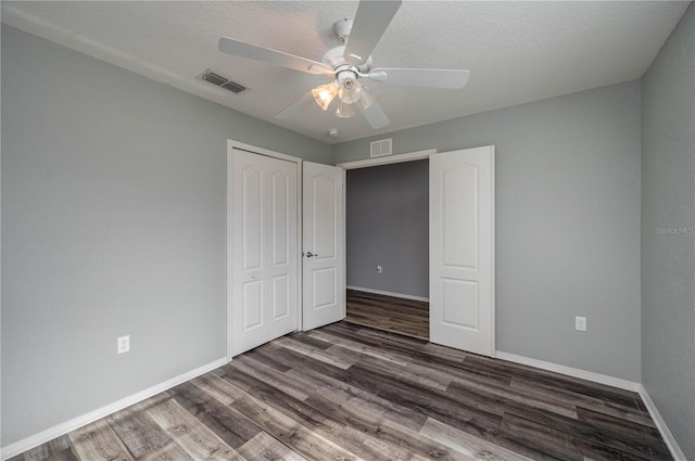 unfurnished bedroom with a textured ceiling, ceiling fan, dark wood-type flooring, and a closet