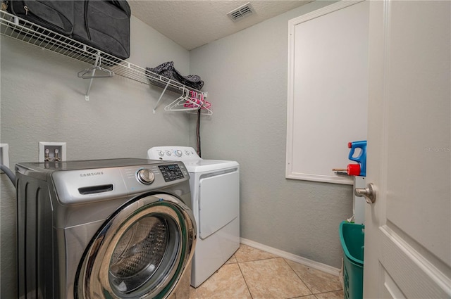 clothes washing area featuring washing machine and clothes dryer, light tile patterned floors, and a textured ceiling