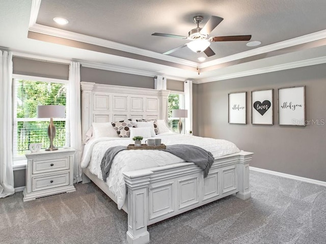 carpeted bedroom with a raised ceiling, multiple windows, crown molding, and ceiling fan