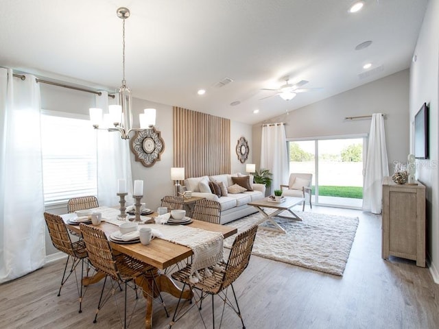 dining area with ceiling fan with notable chandelier, lofted ceiling, and light wood-type flooring