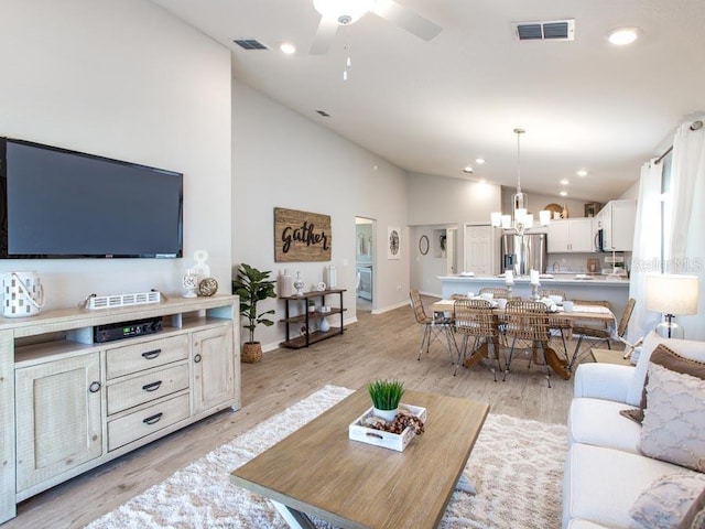 living room with ceiling fan with notable chandelier, high vaulted ceiling, and light hardwood / wood-style flooring