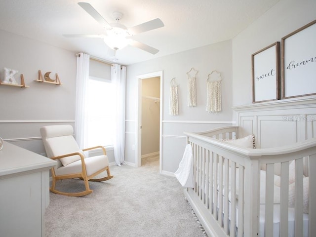 bedroom with ceiling fan, a spacious closet, a nursery area, light colored carpet, and a closet