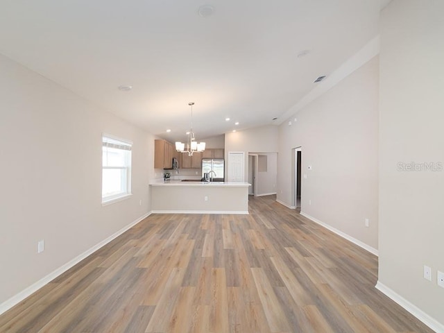 unfurnished living room featuring lofted ceiling, a chandelier, and light wood-type flooring