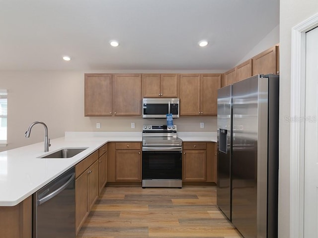 kitchen featuring sink, light hardwood / wood-style floors, kitchen peninsula, and appliances with stainless steel finishes