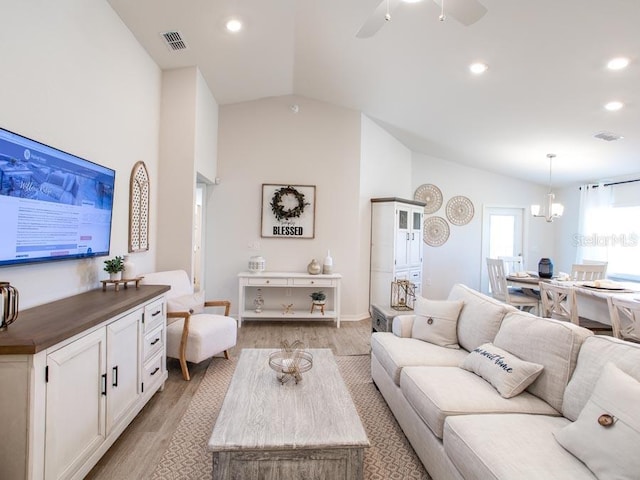 living room with ceiling fan with notable chandelier, light hardwood / wood-style flooring, and vaulted ceiling