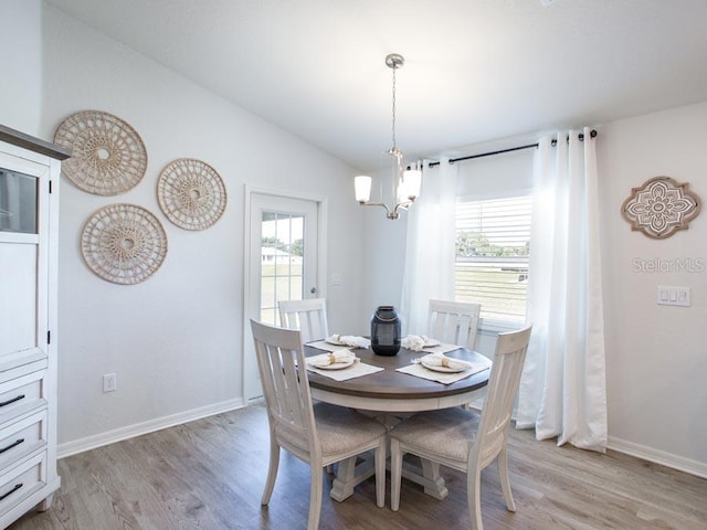 dining room with light hardwood / wood-style floors, vaulted ceiling, and a notable chandelier