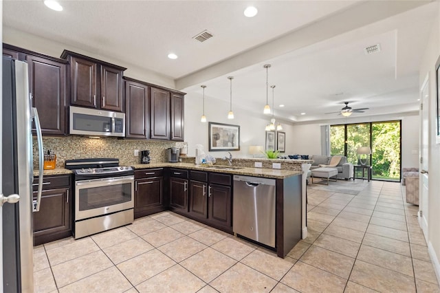 kitchen featuring kitchen peninsula, light stone counters, stainless steel appliances, ceiling fan, and hanging light fixtures