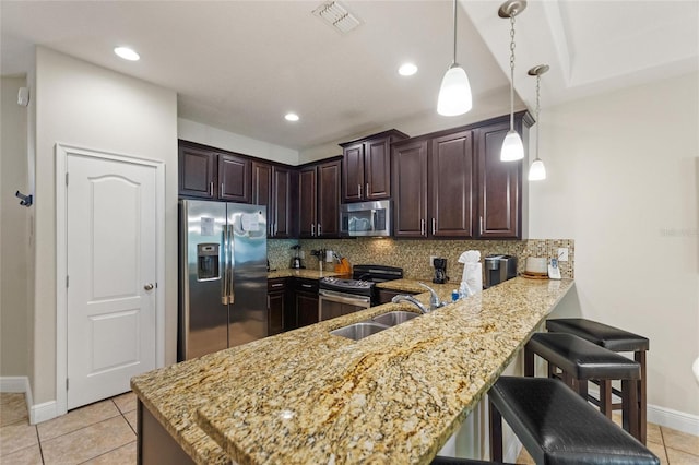 kitchen with a breakfast bar, hanging light fixtures, appliances with stainless steel finishes, tasteful backsplash, and kitchen peninsula