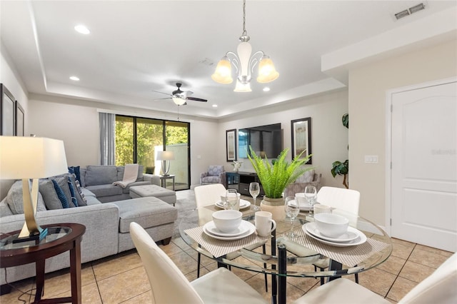 tiled living room with ceiling fan with notable chandelier and a raised ceiling