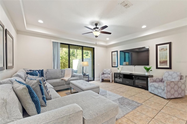 living room with a tray ceiling, ceiling fan, and light tile patterned floors