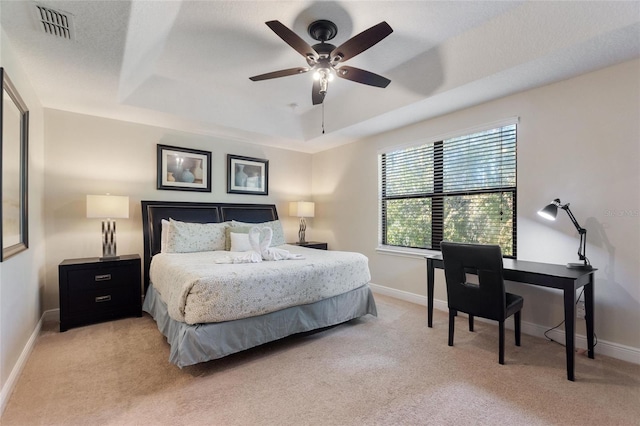 bedroom with a raised ceiling, ceiling fan, and light carpet