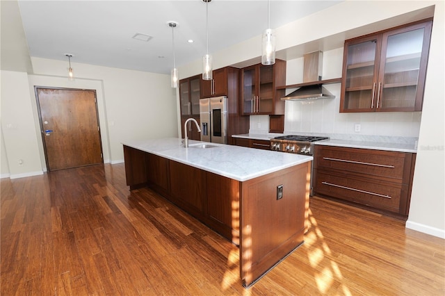 kitchen with backsplash, a center island with sink, hardwood / wood-style flooring, appliances with stainless steel finishes, and decorative light fixtures