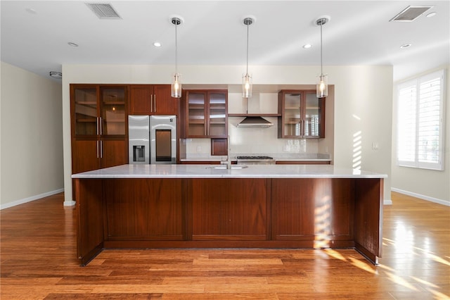 kitchen with stainless steel fridge with ice dispenser, pendant lighting, wall chimney range hood, and light wood-type flooring