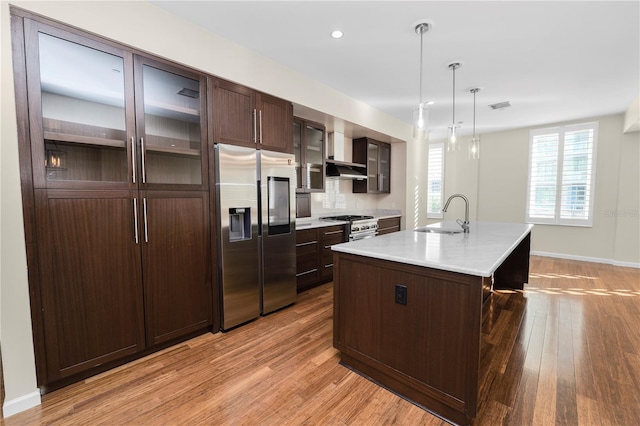 kitchen featuring sink, an island with sink, decorative light fixtures, high quality appliances, and light wood-type flooring