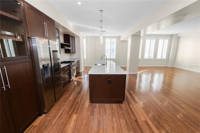 kitchen featuring appliances with stainless steel finishes, dark hardwood / wood-style flooring, sink, hanging light fixtures, and an island with sink