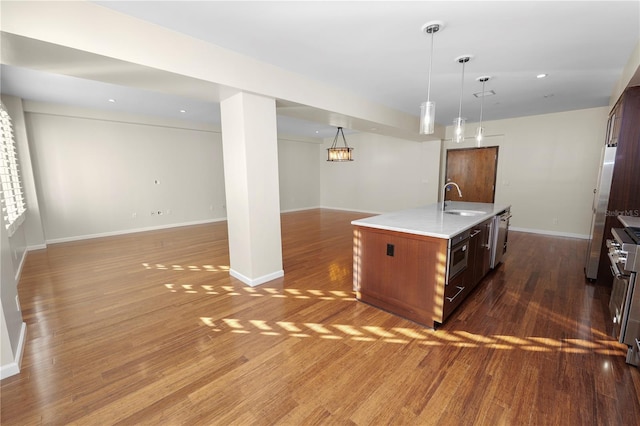 kitchen with appliances with stainless steel finishes, sink, pendant lighting, a center island with sink, and dark hardwood / wood-style floors