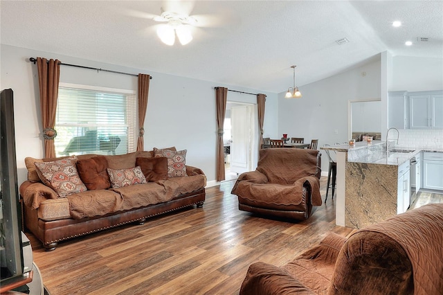 living room featuring ceiling fan with notable chandelier, sink, light hardwood / wood-style flooring, vaulted ceiling, and a textured ceiling