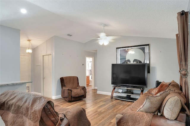 living room with ceiling fan with notable chandelier, a textured ceiling, light hardwood / wood-style floors, and vaulted ceiling