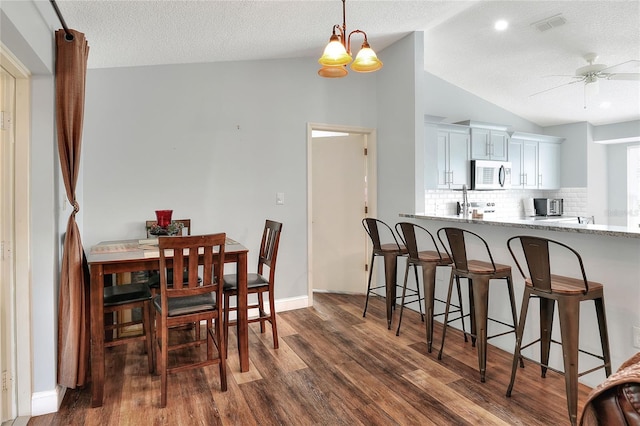 dining space featuring a textured ceiling, ceiling fan with notable chandelier, dark wood-type flooring, and vaulted ceiling