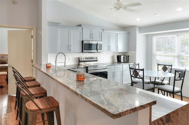 kitchen with light wood-type flooring, a textured ceiling, appliances with stainless steel finishes, and vaulted ceiling