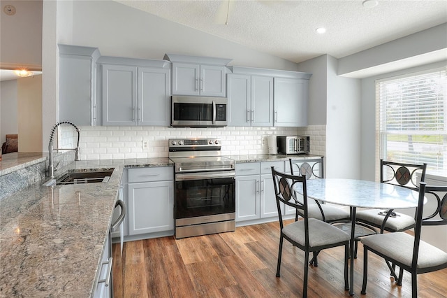 kitchen featuring appliances with stainless steel finishes, a textured ceiling, sink, light hardwood / wood-style flooring, and lofted ceiling