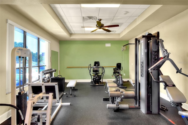 workout area with a paneled ceiling, a raised ceiling, and ceiling fan