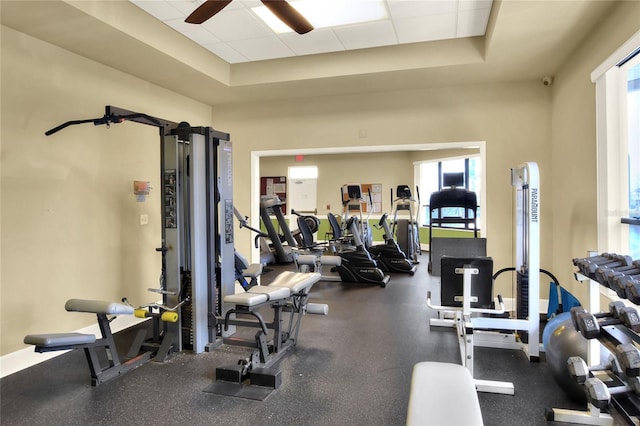 exercise room with a paneled ceiling, ceiling fan, and a raised ceiling