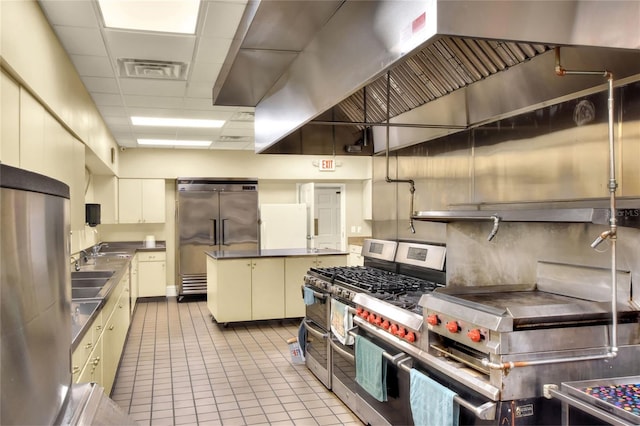 kitchen with a paneled ceiling, a center island, wall chimney range hood, sink, and appliances with stainless steel finishes