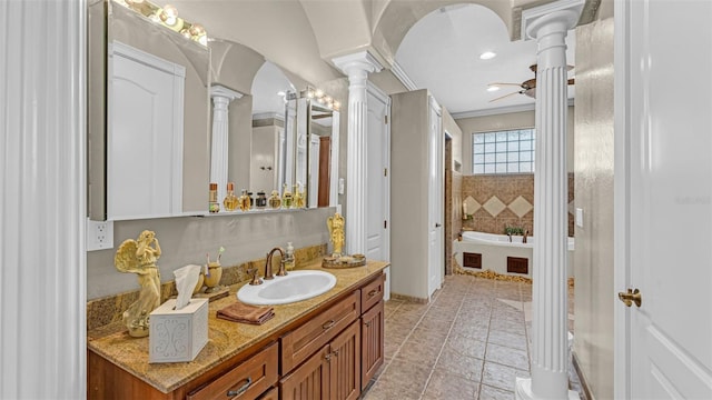 bathroom with a bathing tub, ceiling fan, decorative columns, vanity, and ornamental molding