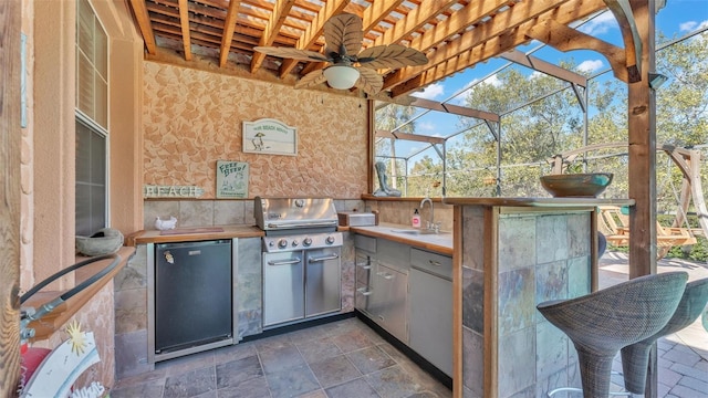 view of patio with an outdoor kitchen, area for grilling, ceiling fan, sink, and glass enclosure