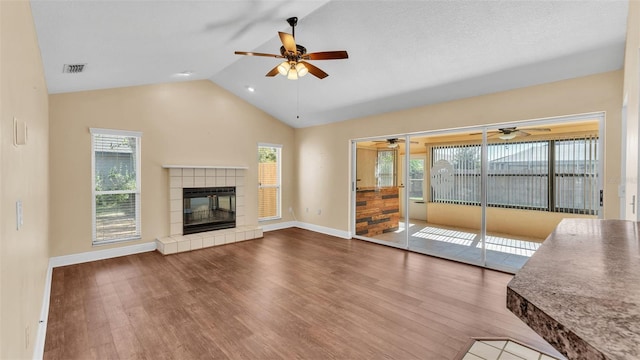 unfurnished living room with lofted ceiling, visible vents, a tiled fireplace, wood finished floors, and baseboards