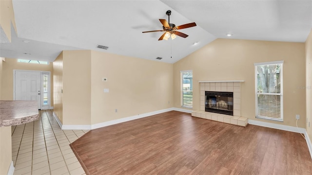 unfurnished living room with a wealth of natural light, visible vents, lofted ceiling, and a tile fireplace