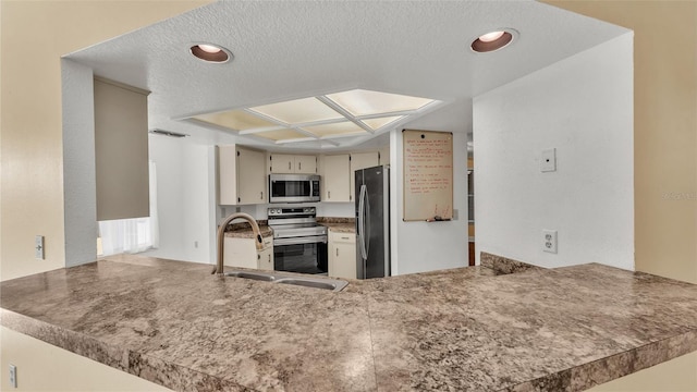 kitchen featuring a peninsula, a textured ceiling, stainless steel appliances, and a sink