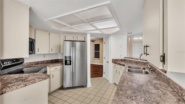 kitchen with a textured ceiling, appliances with stainless steel finishes, cream cabinets, and a sink