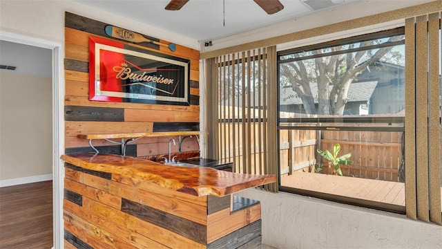 dining space featuring ceiling fan, wooden walls, baseboards, and wood finished floors