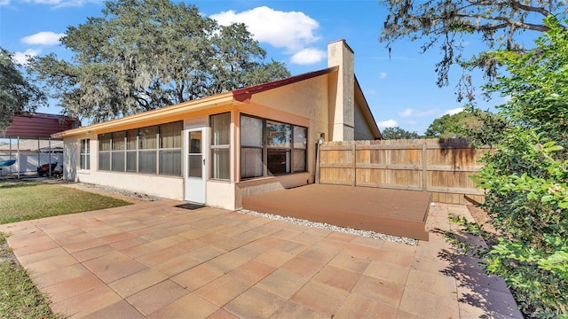 rear view of property featuring a patio, a chimney, stucco siding, a sunroom, and fence