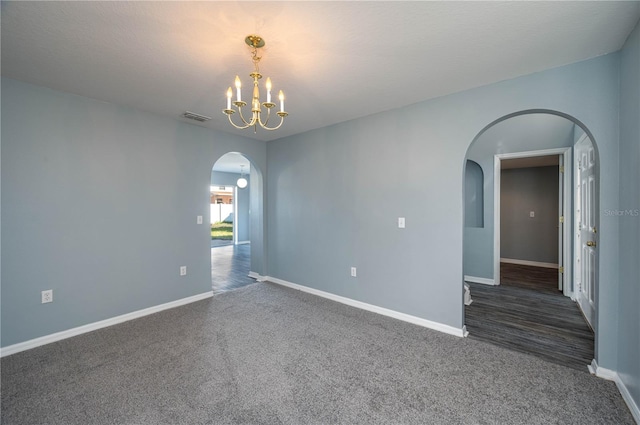 empty room featuring dark colored carpet and a notable chandelier