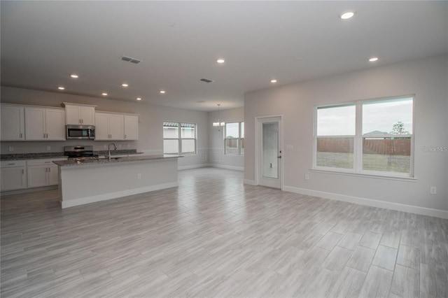 kitchen with appliances with stainless steel finishes, a kitchen island with sink, sink, dark stone countertops, and white cabinetry