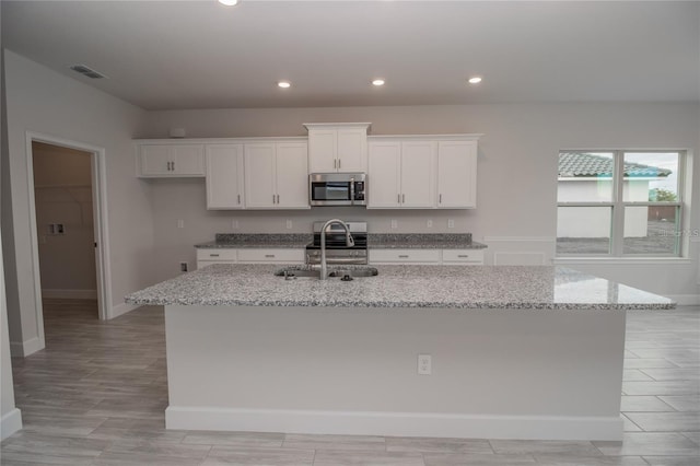 kitchen with white cabinetry, a center island with sink, light stone countertops, and appliances with stainless steel finishes