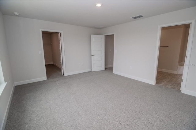 unfurnished bedroom with a spacious closet, a closet, and light colored carpet