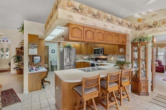 kitchen with kitchen peninsula, appliances with stainless steel finishes, sink, light tile patterned floors, and a breakfast bar area