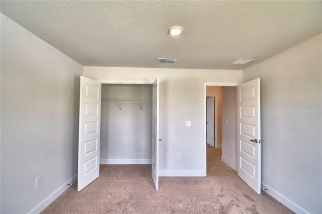 unfurnished bedroom featuring light colored carpet, a textured ceiling, and a closet