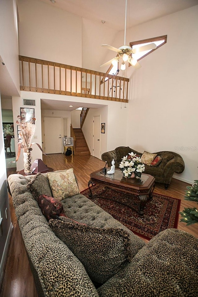 living room with wood finished floors, visible vents, a towering ceiling, a ceiling fan, and stairway