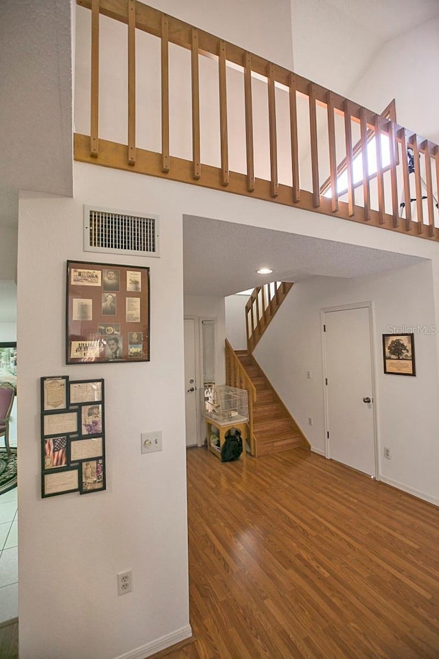 interior space featuring high vaulted ceiling, wood finished floors, visible vents, baseboards, and stairway