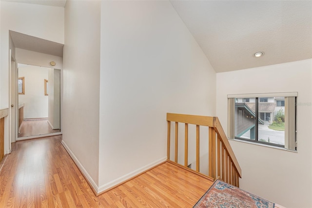 corridor featuring baseboards, light wood-style flooring, and an upstairs landing