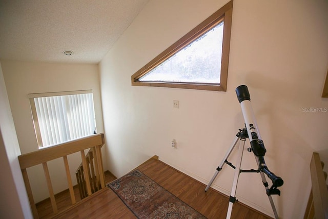 corridor with a textured ceiling, wood finished floors, and an upstairs landing